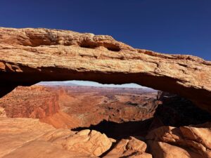 The through the window of a massive arch at Canyonlands an expansive landscape of pillar, buttes and mesas is shown.